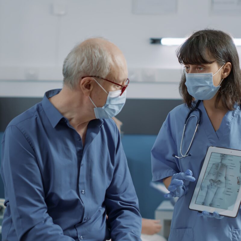 Doctor showing an X-ray to an elderly patient at home, highlighting post-acute care.